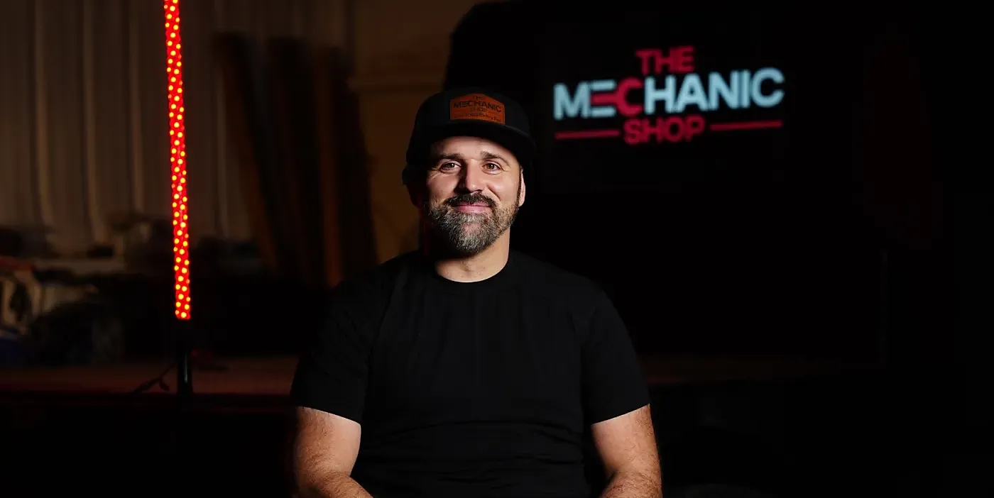 Steve, owner of The Mechanic Shop in Amarillo, TX, in front of the neon shop sign